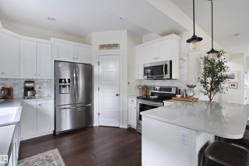 Contemporary kitchen featuring white cabinetry, stainless steel appliances, light-toned countertops, wood-finish flooring, and recessed lighting - 34 Falcon Road, Cold Lake, AB 
