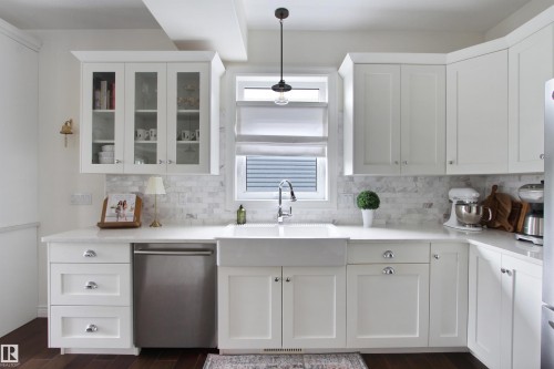 Kitchen featuring white shaker-style cabinetry, a farmhouse sink with a gooseneck faucet, white countertops, and a full-height tile backsplash - 34 Falcon Road, Cold Lake, AB 