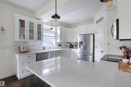 Modern kitchen featuring white cabinetry, a large kitchen island with a light-toned countertop, stainless steel appliances, a farmhouse sink, and marble subway tile backsplash - 34 Falcon Road, Cold Lake, AB 