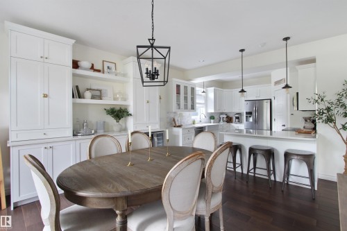 Open-concept kitchen and dining area featuring dark wood-finish flooring, a white kitchen island with seating, pendant lighting, stainless steel appliances, and white cabinetry - 34 Falcon Road, Cold Lake, AB 