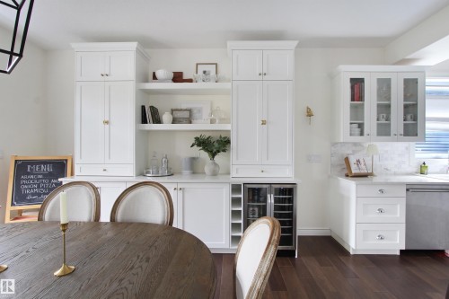 Built-in white cabinetry with gold-tone hardware, integrated wine refrigerator, open shelving, and wood-finish flooring - 34 Falcon Road, Cold Lake, AB 