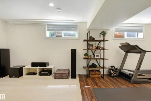 Finished basement space featuring recessed lighting, two windows with blinds, a white media console, and a built-in shelving unit with black metal framing and wood-finish shelves - 34 Falcon Road, Cold Lake, AB 