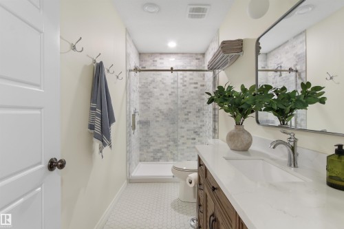 Bathroom featuring a wood-finish vanity with a white countertop and integrated sink, a large framed mirror, and a walk-in shower with glass enclosure and mosaic tile surround - 34 Falcon Road, Cold Lake, AB 