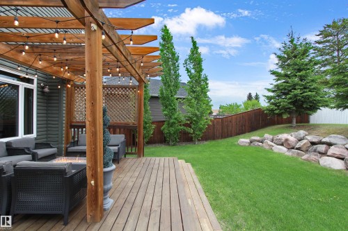 Spacious wood-finish deck with a custom pergola, featuring wood lattice privacy screens and an integrated string lighting system - 34 Falcon Road, Cold Lake, AB 