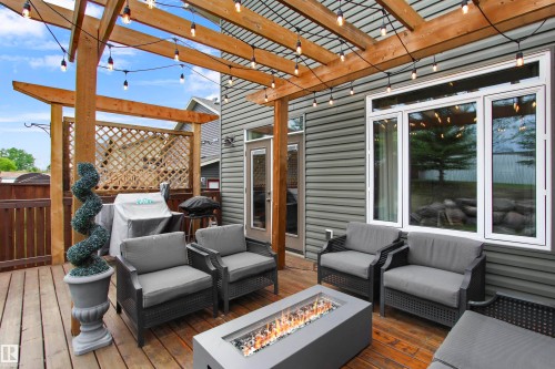 Spacious wood-finish deck with a wood pergola, string lights, a fire pit, and gray siding exterior - 34 Falcon Road, Cold Lake, AB 