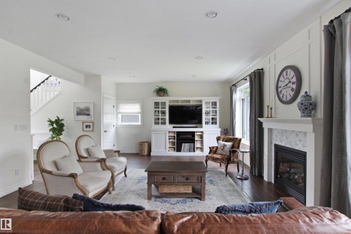 Spacious living area featuring dark wood-finish flooring, a built-in media center with integrated shelving, and a white mantel fireplace with a patterned tile surround - 34 Falcon Road, Cold Lake, AB 