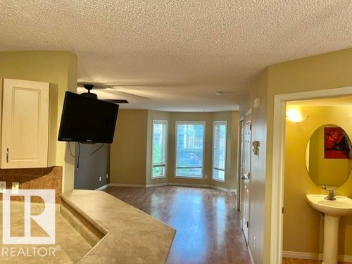 Open concept living area with wood-finish flooring, bay windows, a ceiling fan, and built-in cabinetry - 1 5281 Terwillegar Boulevard, Edmonton, AB 