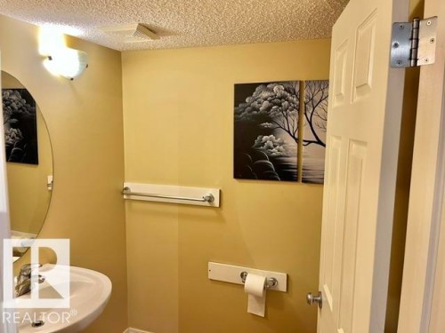 Pedestal sink with chrome faucet, complemented by an oval mirror and wall-mounted light fixture - 1 5281 Terwillegar Boulevard, Edmonton, AB 