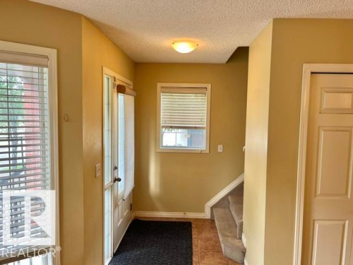 Foyer featuring a paneled entry door with sidelights, tiled flooring, an overhead flush-mount light fixture, and carpeted stairs - 1 5281 Terwillegar Boulevard, Edmonton, AB 