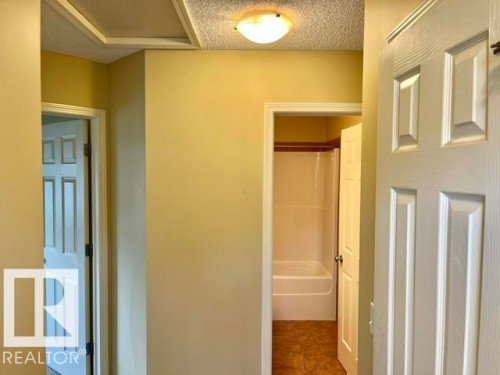 Hallway featuring panel doors, a flush-mount light fixture, and textured ceilings - 1 5281 Terwillegar Boulevard, Edmonton, AB 