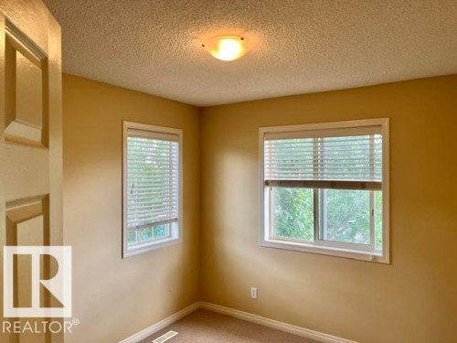 Bright room featuring two windows with white blinds, neutral painted walls, textured ceiling, and a ceiling-mounted light fixture - 1 5281 Terwillegar Boulevard, Edmonton, AB 