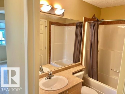 Bathroom featuring a single vanity with an integrated sink, a rectangular mirror, and an overhead light fixture - 1 5281 Terwillegar Boulevard, Edmonton, AB 