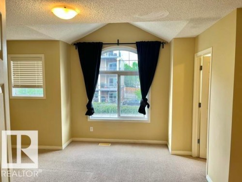 Room featuring an arched window, a secondary rectangular window with blinds, and beige carpeting - 1 5281 Terwillegar Boulevard, Edmonton, AB 