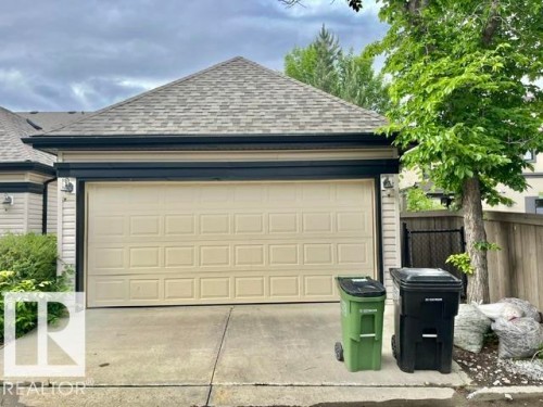 Attached garage featuring a panel-style door, concrete driveway, and exterior wall lighting fixtures - 1 5281 Terwillegar Boulevard, Edmonton, AB 