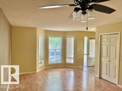 Living area featuring wood-finish flooring, a bay window with multiple vertical windows, a ceiling fan with integrated lighting, and a bi-fold closet door - 