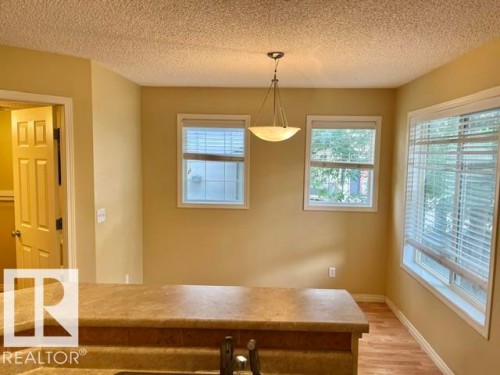 Dining area featuring a contemporary pendant light fixture, three windows with white blinds, and wood-finish flooring - 1 5281 Terwillegar Boulevard, Edmonton, AB 