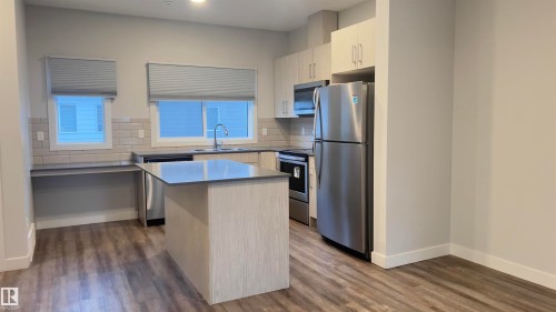 Kitchen featuring a central island with countertop seating, stainless steel appliances, light wood-finish cabinetry, a subway tile backsplash, and wood-finish flooring - 90 804 Welsh Drive, Edmonton, AB 