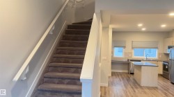 Carpeted staircase with white handrail leading to an open-concept kitchen - 