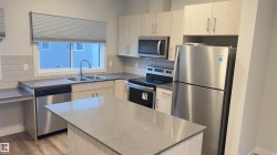 Modern kitchen featuring light wood-finish cabinetry, stainless steel appliances, a center island, and wood-finish flooring - 