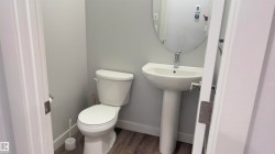 Pedestal sink with chrome faucet, oval mirror, and wood-finish flooring - 
