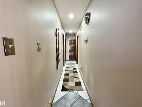 Hallway featuring light neutral wall paint, recessed ceiling lighting, wood doors, and square floor tiles - 11031 166 Avenue, Edmonton, AB 