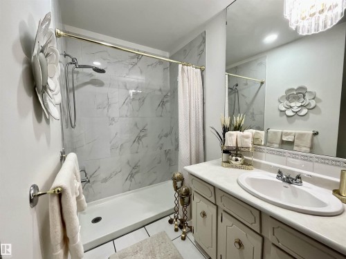 Updated bathroom featuring a walk-in shower with marble-look tile surround and a gold-finish shower rod - 11031 166 Avenue, Edmonton, AB 
