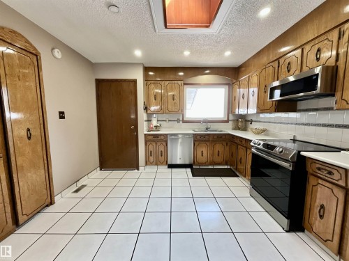 Kitchen featuring wood cabinetry, white tile flooring, stainless steel appliances, and a skylight - 11031 166 Avenue, Edmonton, AB 