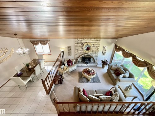 Open-concept living space featuring a wood-panel ceiling, stone fireplace with hearth, and extensive natural light - 11031 166 Avenue, Edmonton, AB 