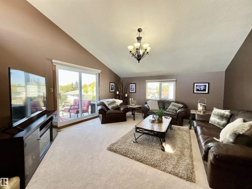 Living area featuring vaulted ceilings, light-colored carpeting, a multi-light chandelier, and a sliding glass door opening to an outdoor deck - 11031 166 Avenue, Edmonton, AB 