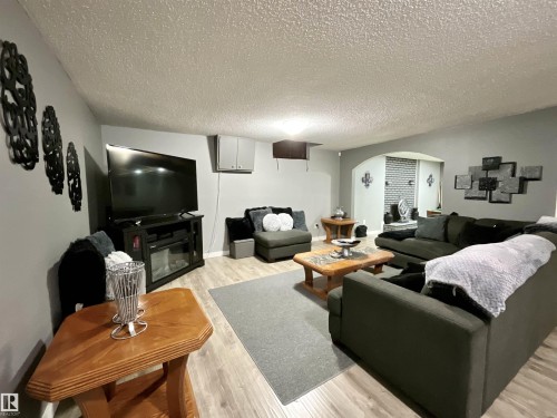 Spacious recreation room featuring wood-finish flooring, light gray walls, an arched entryway, recessed lighting, and a built-in media console with an electric fireplace - 11031 166 Avenue, Edmonton, AB 