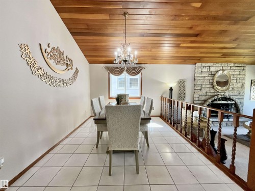 Dining area featuring an elaborate chandelier, a wood-paneled ceiling, white tile flooring, a window with a valance, and a decorative wood railing - 11031 166 Avenue, Edmonton, AB 