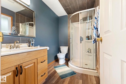 Bathroom featuring a wood-finish vanity with an integrated sink, brushed nickel faucet, and a large mirror - 9940 83 St, Fort Saskatchewan, AB 