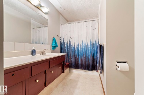 Bathroom featuring a single vanity with a white countertop, a recessed sink, and a large mirror - 9940 83 St, Fort Saskatchewan, AB 