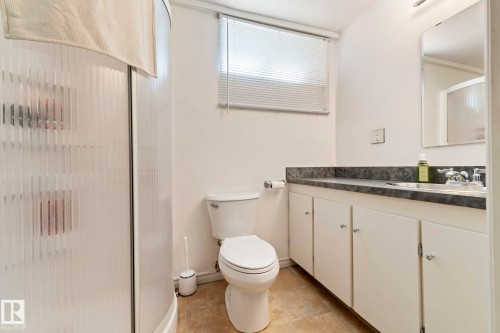 Bathroom featuring a standing shower with privacy glass, a white toilet, and a vanity with a dark countertop, integrated sink, and white cabinetry - 9940 83 St, Fort Saskatchewan, AB 