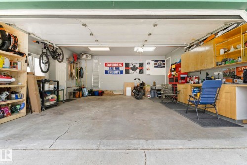 Spacious garage featuring a concrete floor, built-in wooden shelving, overhead lighting, and extensive wall-mounted cabinetry - 9940 83 St, Fort Saskatchewan, AB 
