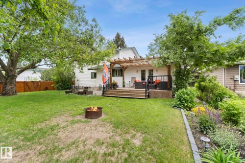 Expansive backyard featuring a wood deck with black metal railings, a wood pergola, and mature trees - 9940 83 St, Fort Saskatchewan, AB 