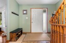 Entryway featuring a white paneled door with a frosted sidelight, wood-finish flooring, and a natural wood staircase with balusters - 9940 83 St, Fort Saskatchewan, AB 