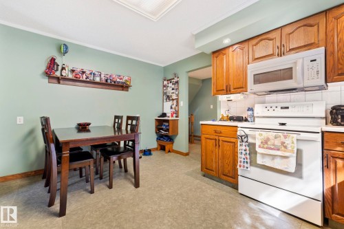 Kitchen dining area featuring a built-in wooden shelf, wood-finish cabinetry, white countertop, white tile backsplash, and built-in microwave above a white range - 9940 83 St, Fort Saskatchewan, AB 