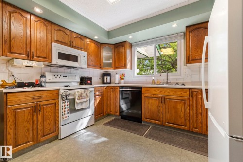 Kitchen featuring wood-finish cabinetry, white appliances, and a tile backsplash - 9940 83 St, Fort Saskatchewan, AB 