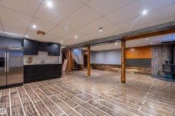Spacious open-concept lower level featuring wood-finish flooring, recessed lighting, and exposed timber columns - 