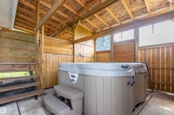 Covered outdoor spa area featuring a hot tub with steps, natural wood paneling, an exposed beam ceiling, and a lattice privacy screen - 