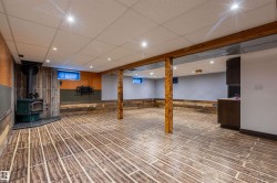 Spacious finished room featuring wood-finish flooring, recessed lighting, and a wood-burning stove with a tile surround - 