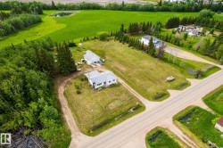 Spacious property featuring two residential structures and a detached garage, set against a backdrop of mature trees and expansive green fields - 