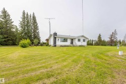 Spacious property featuring a white exterior residence with a black chimney, expansive green lawn, mature evergreen trees, and a clear sky backdrop - 