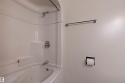 White acrylic tub and shower combination with chrome fixtures, an integrated shelf, and a shower curtain rod - 