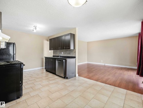 Kitchen area with light-toned tiled flooring, dark wood-finish cabinetry, and a stainless steel dishwasher - 13114 30 Street, Edmonton, AB - Indoor Photo Showing Kitchen