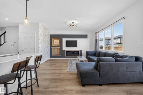 Open-concept living area featuring wood-finish flooring, a contemporary built-in entertainment center with shelving, and large windows providing abundant natural light - 1684 12 Street, Edmonton, AB 