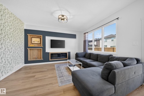 Living area featuring wood-finish flooring, a decorative accent wall, built-in shelving, an integrated fireplace, and a large window - 1684 12 Street, Edmonton, AB 