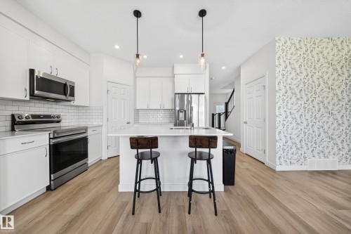Contemporary kitchen featuring a spacious island with pendant lighting, white cabinetry, stainless steel appliances, and wood-finish flooring - 1684 12 Street, Edmonton, AB 
