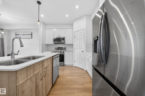 Kitchen featuring a dual-basin stainless steel sink, wood-finish island cabinetry, stainless steel appliances, white subway tile backsplash, and recessed lighting - 1684 12 Street, Edmonton, AB 